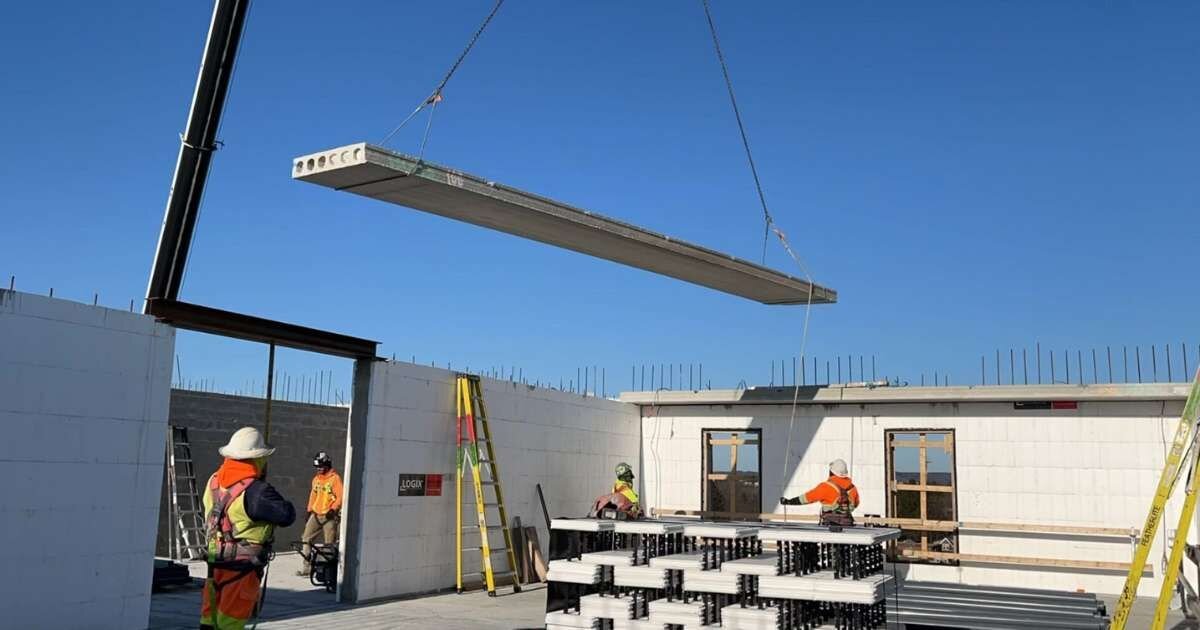 Crain lowering a concrete slab to workers on building construction site 